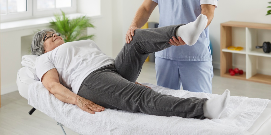 Happy senior woman lying on exam couch while chiropractor, osteopath or physiotherapy specialist is examining her leg and knee. Osteoporosis treatment, physical therapy, remedial exercise concept