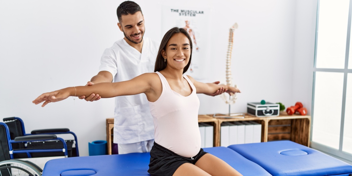 Latin man and woman wearing physiotherapist uniform having pregnancy rehab session at physiotherapy clinic