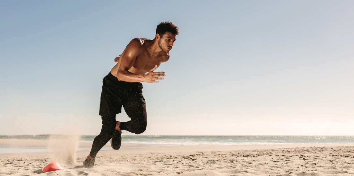 Man doing fitness workout at a beach on a sunny day. Athletic man setting off for a sprint on the beach.