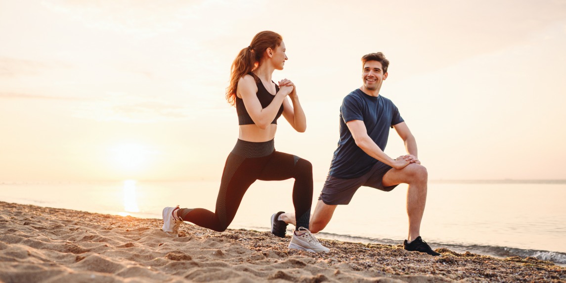 Full size couple young two friend strong sporty sportswoman sportsman woman man in sport clothes warm up training do lunges do exercise on sand sea ocean beach outdoor on seaside in summer day morning