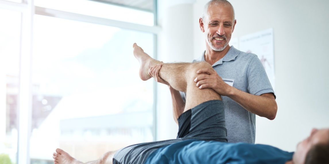 Healthcare, physiotherapist and patient with leg injury, stretching and recovery with treatment, healing or care. Male person, employee or chiropractor with a client, physical therapy or consultation