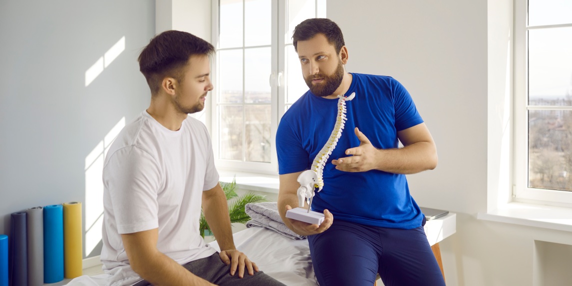 Man professional osteopath chiropractor is consulting man showing him spine layout in hospital. They talking about backbone problems. Checkup, prevention examination, diagnosis, medicine concept.