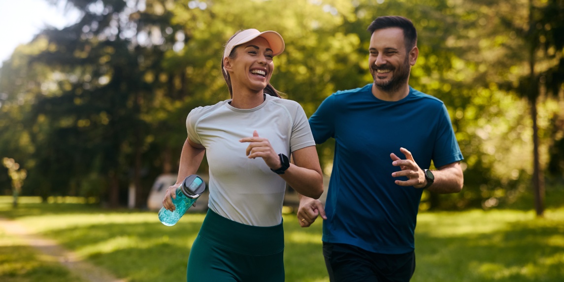 Happy athletic couple having fun while running together in nature. Copy space.